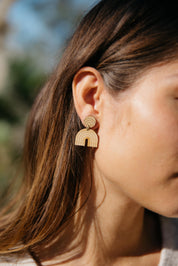 Close-up of a person wearing a lightweight rainbow arch-shaped drop earring with a blurred natural background