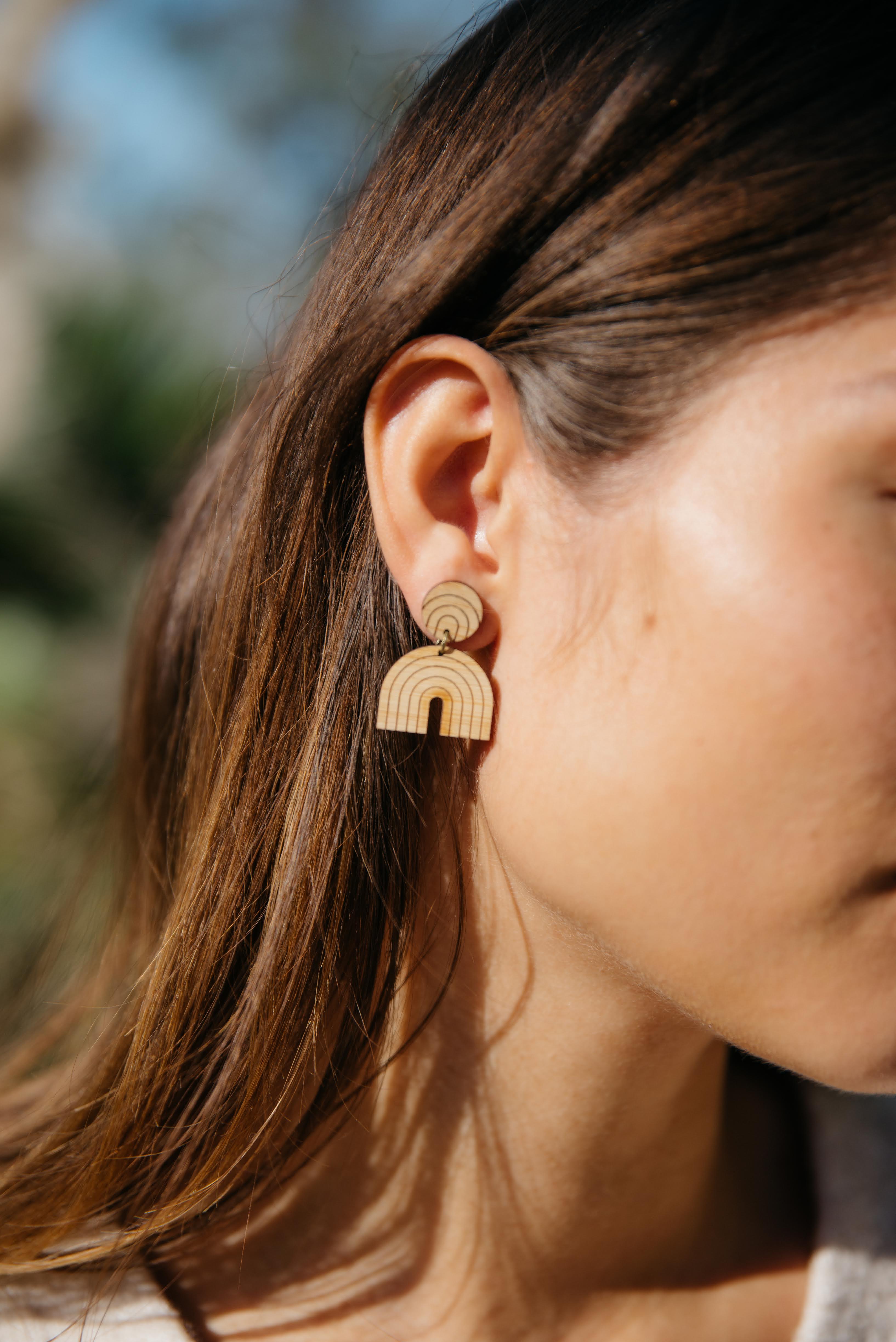 Close-up of a person wearing a lightweight rainbow arch-shaped drop earring with a blurred natural background