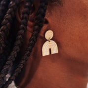 Wooden arch-shaped rainbow drop earrings on a person's ear with braided hair.