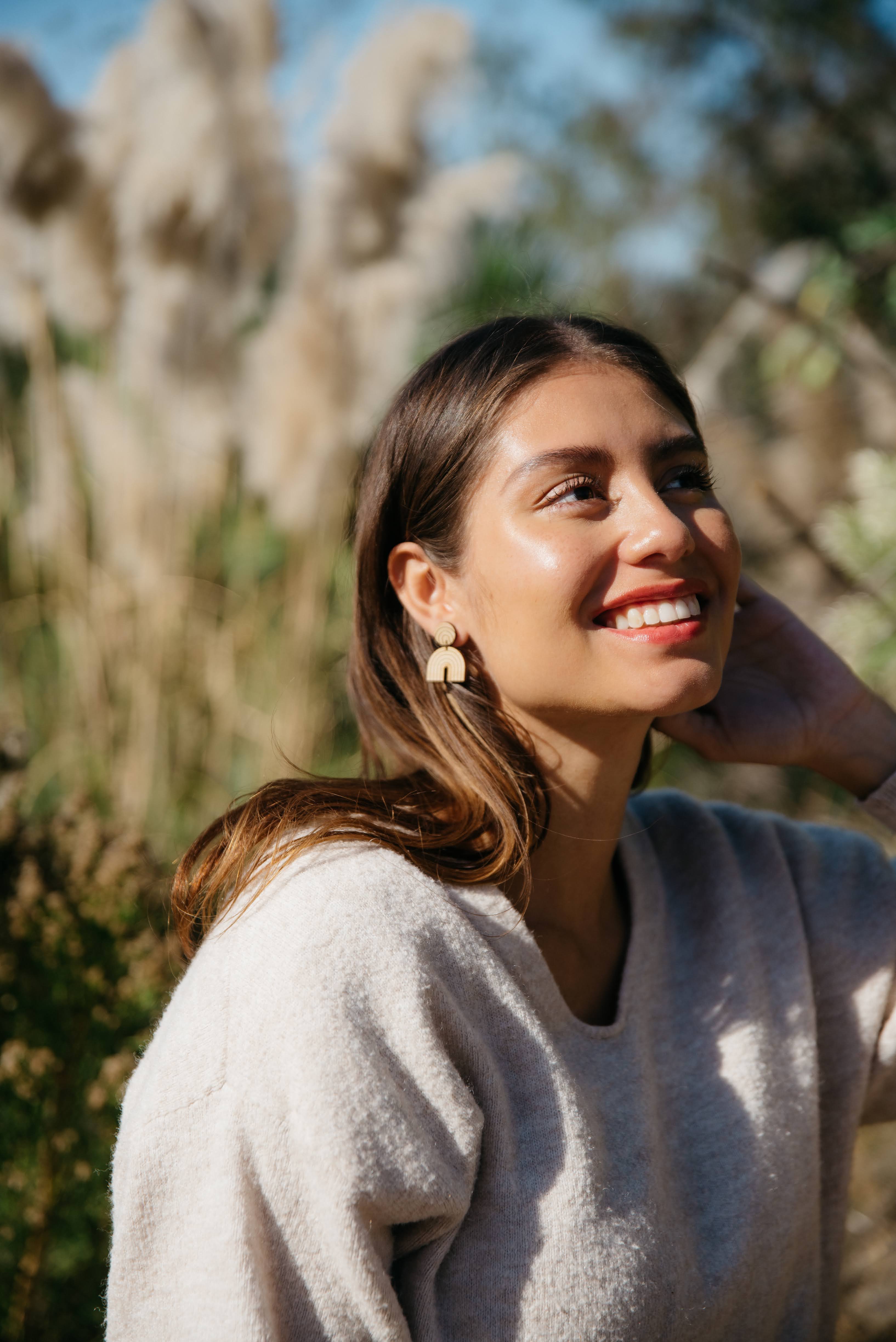 Woman wearing rainbow minimalist bamboo laser cut earrings, smiling outdoors with natural background