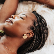 Woman wearing rainbow minimalist drop earring with braided hair lying down on a soft surface