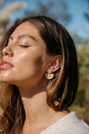 Woman wearing rainbow drop wooden sustainable earrings with a blurred natural background