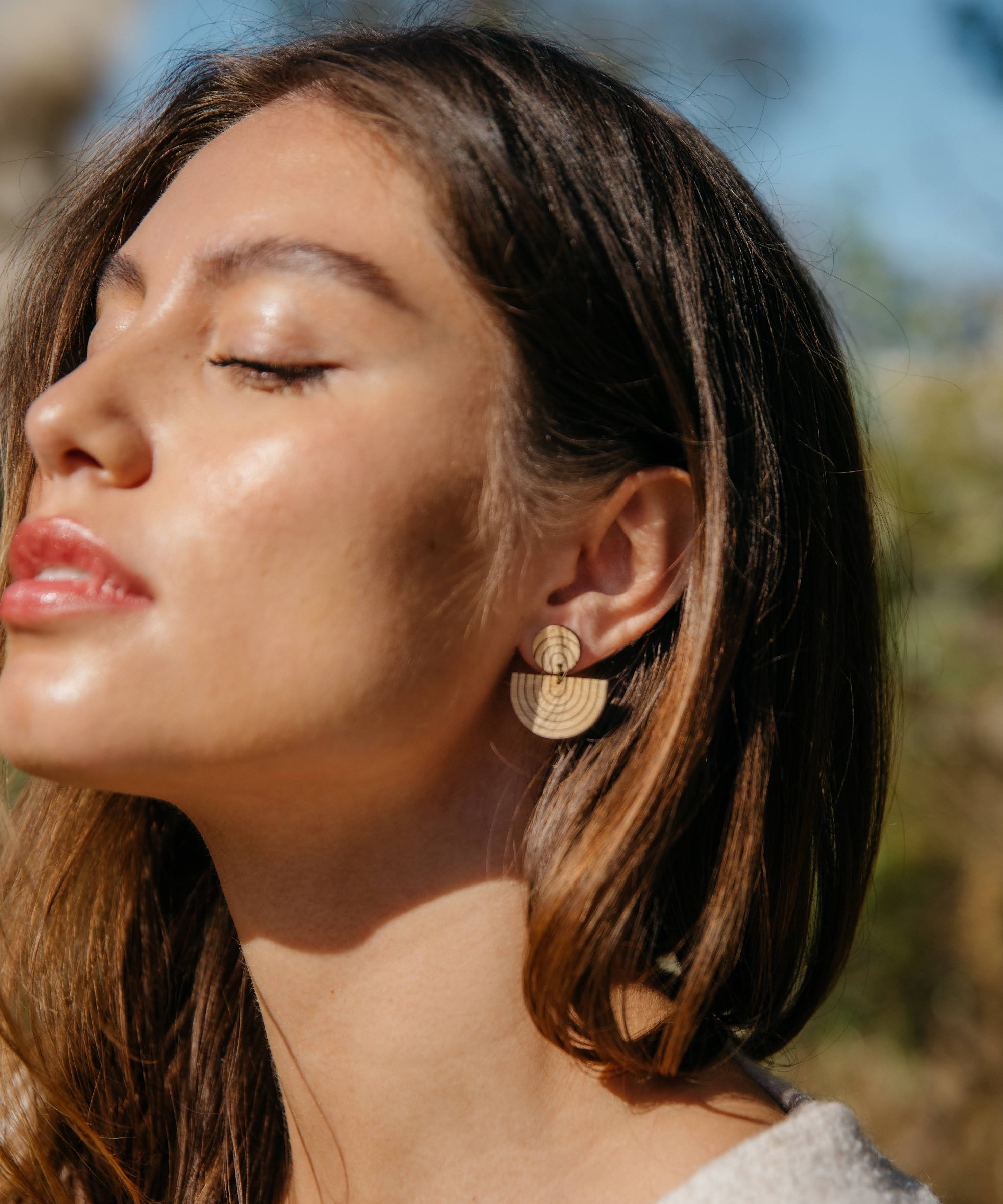 Woman wearing rainbow drop wooden sustainable earrings with a blurred natural background