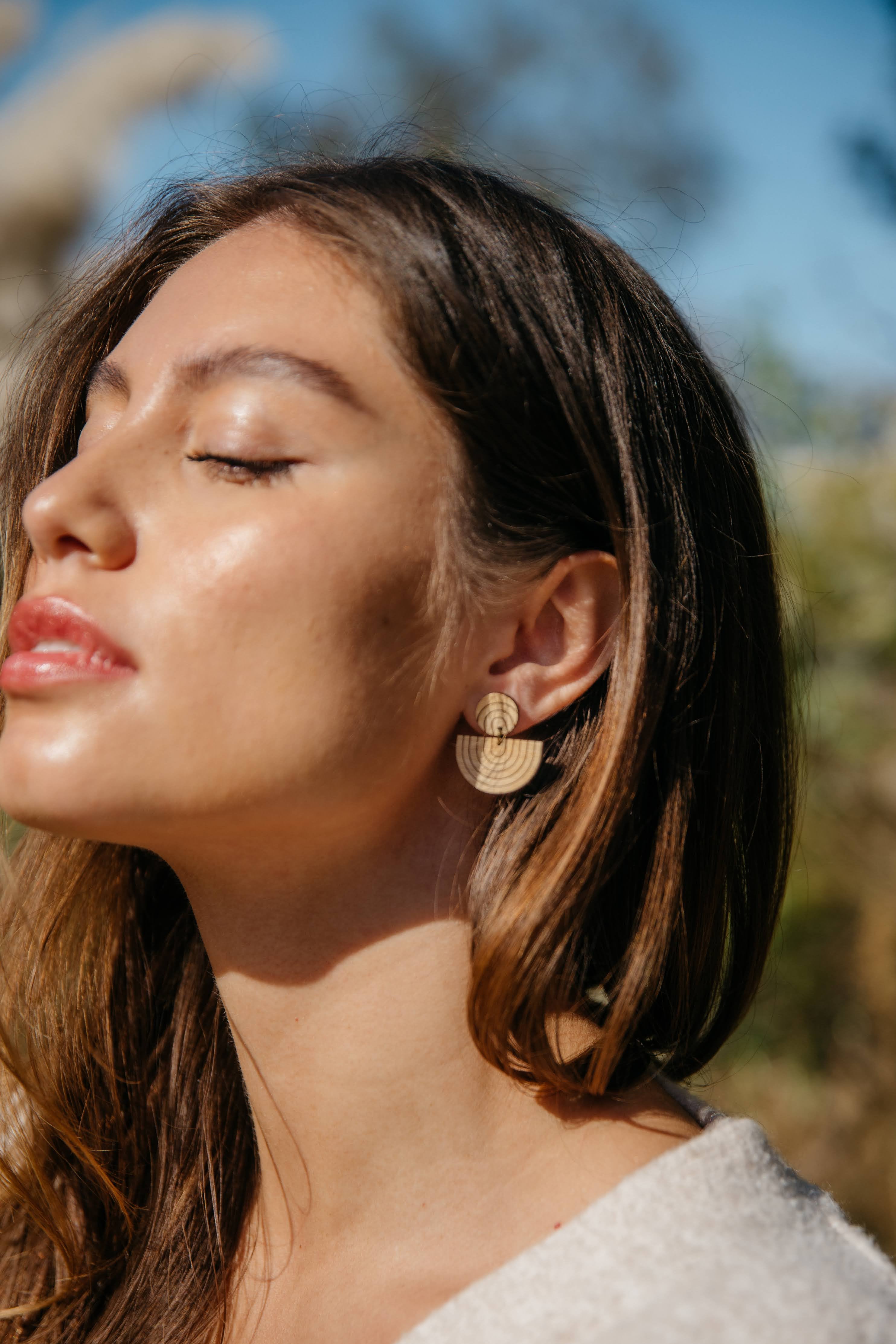 Woman wearing rainbow drop wooden sustainable earrings with a blurred natural background
