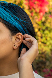 Person with blue hair adjusting a roadrunner wood earring outdoors
