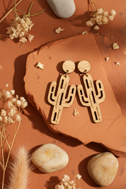 Bamboo cactus-shaped earrings on a textured orange surface with stones and dried plants.
