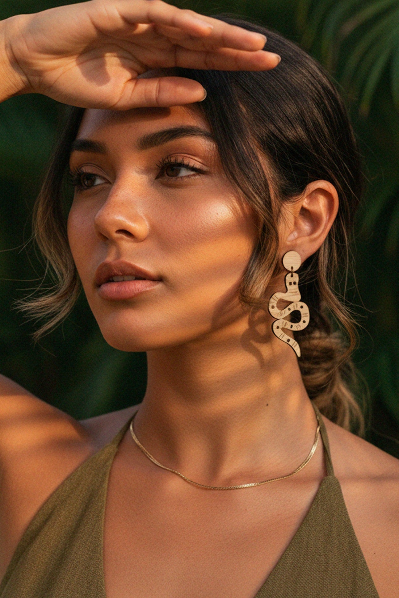 Woman in snake dangles earrings with a green dress with a blurred natural background