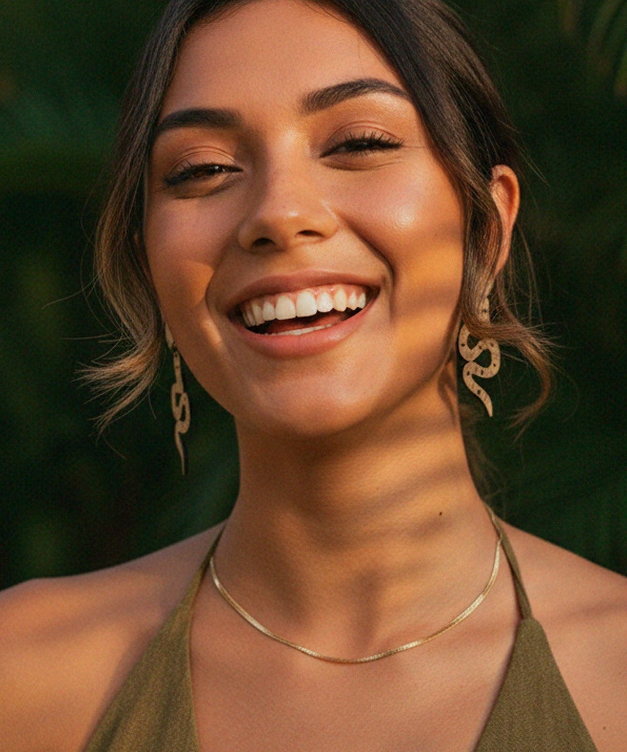 Woman smiling with a snake dangle earrings natural background