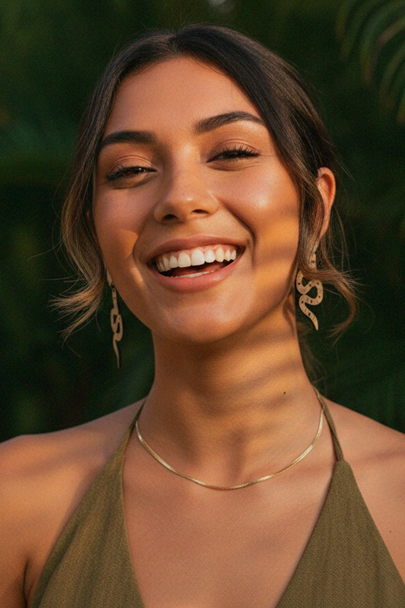 Woman smiling with a snake dangle earrings natural background