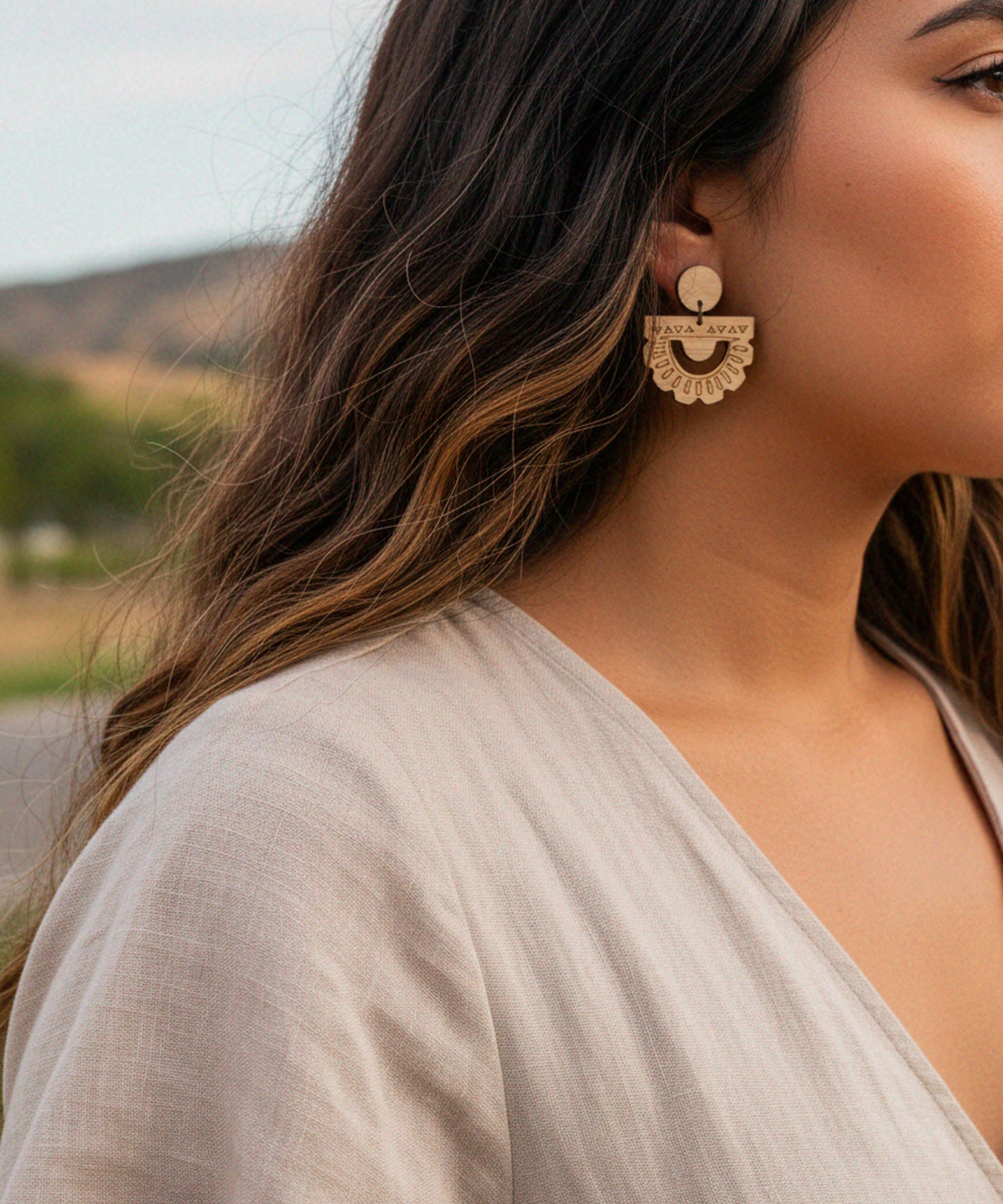 Close-up of a woman wearing handmade laser cut bamboo sun rays earrings with a blurred natural background