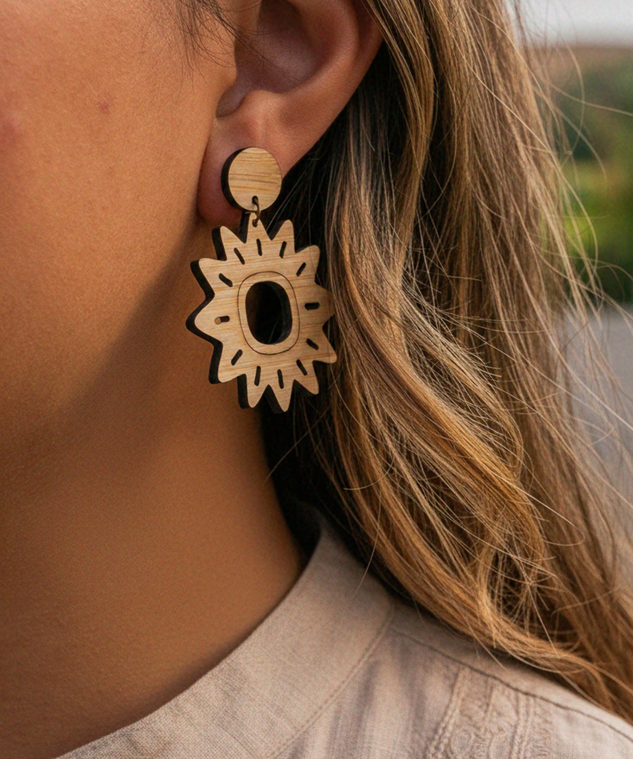 Close-up of a person wearing a sun-shaped wooden laser cut earring.