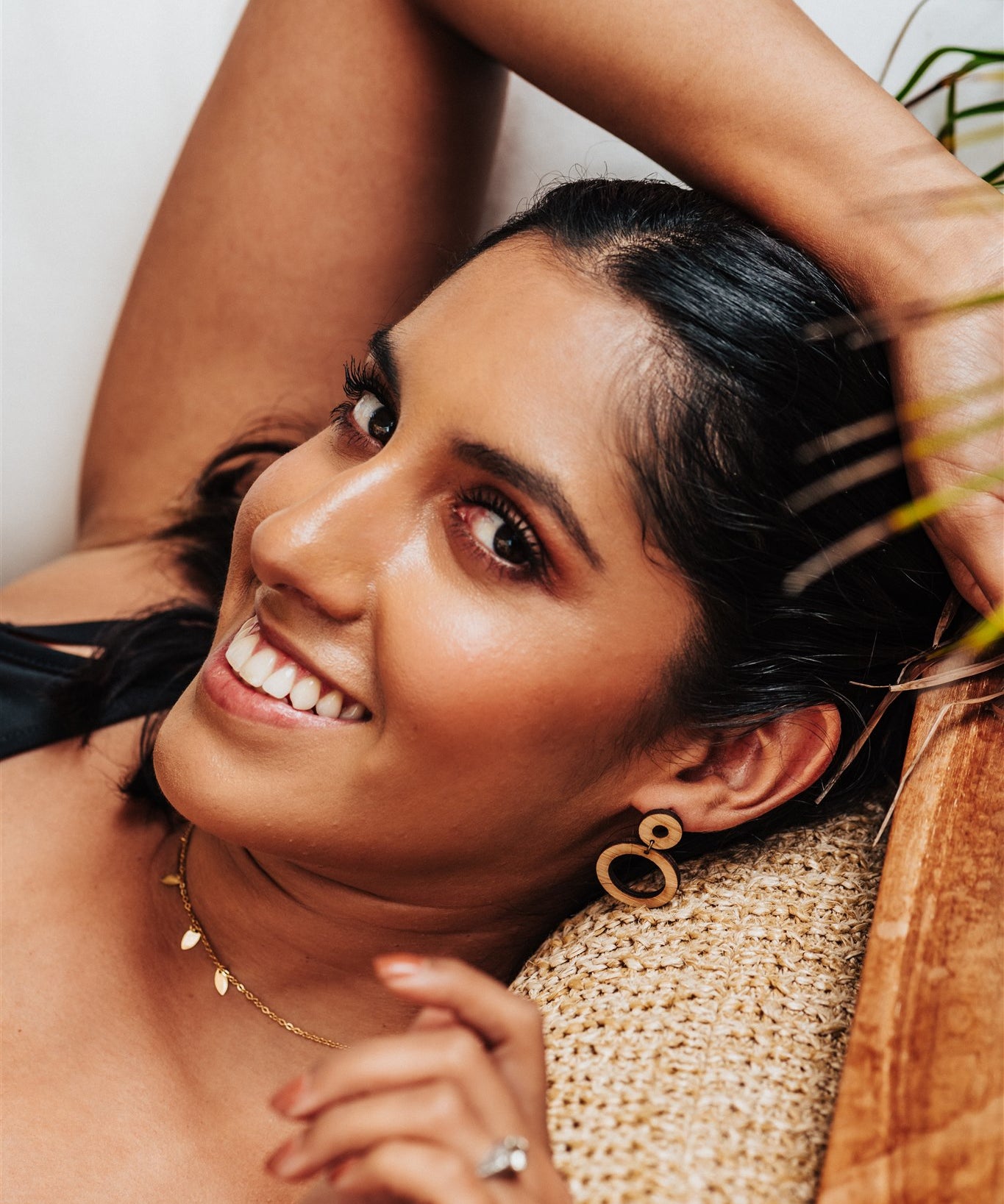 wood hoops earrings worn by a Woman lying on a woven surface with a neutral background