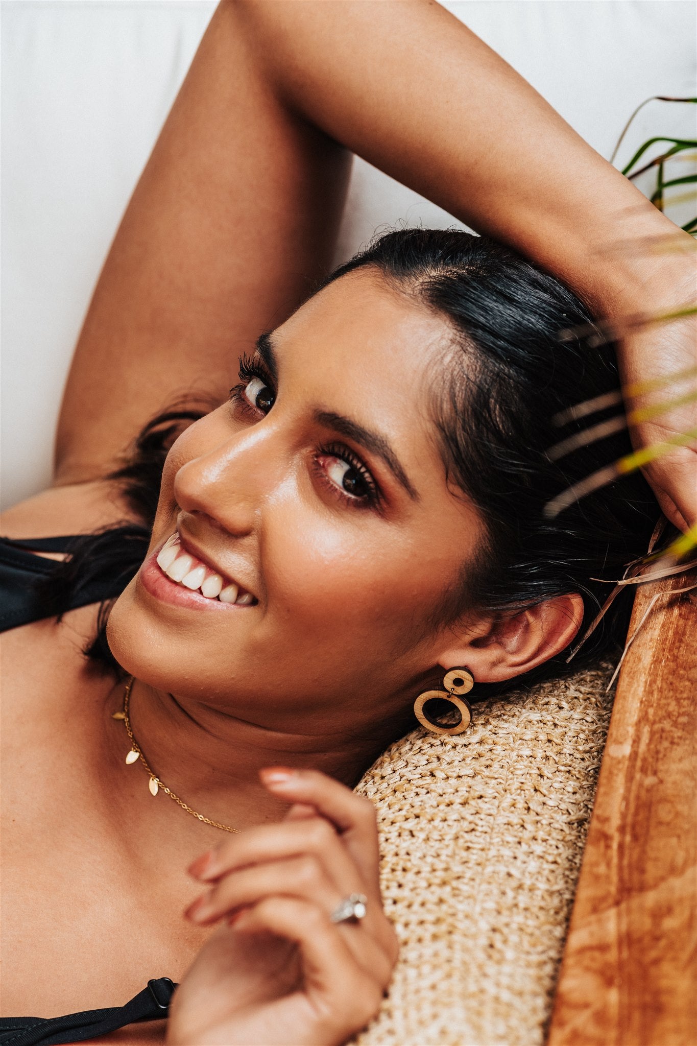 wood hoops earrings worn by a Woman lying on a woven surface with a neutral background
