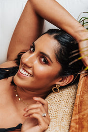 wood hoops earrings worn by a Woman lying on a woven surface with a neutral background