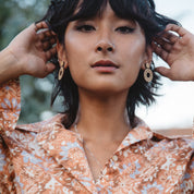 Woman wearing wooden drop circle cut outs earrings with a blurred natural background