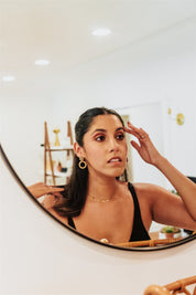 minimalist bamboo hoops earrings dangles worn by a woman adjusting her hair in front of a mirror